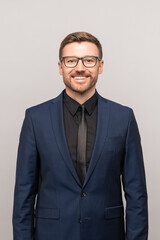 Successful trader guy smiling looks at camera. Happy businessman manager director of large big company, prosperous employee in dark blue business suit. Studio portrait isolated on gray background.