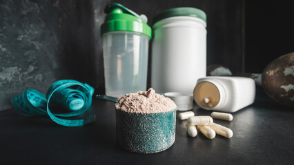Chocolate whey protein powder in measuring spoon, white capsules of amino acids and vitamins,...