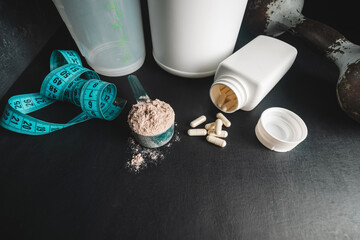 Chocolate whey protein powder in measuring spoon, white capsules of amino acids and vitamins,...