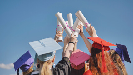 Graduates raise up their diplomas standing together.