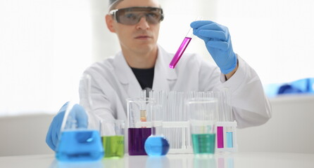 Fototapeta premium A male chemist holds test tube of glass in his hand overflows a liquid solution of potassium permanganate. Conducts an analysis reaction takes various versions of reagents using chemical manufacturing