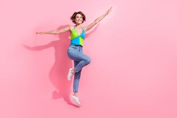 Full length photo of flying jumping sportive fit girl good mood carefree wear hipster outfit summertime isolated on pink color background