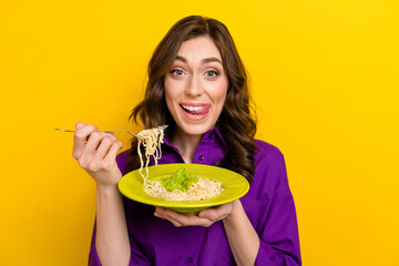 Portrait of excited cheerful person tongue lick teeth hands hold fork spaghetti plate isolated on yellow color background - obrazy, fototapety, plakaty