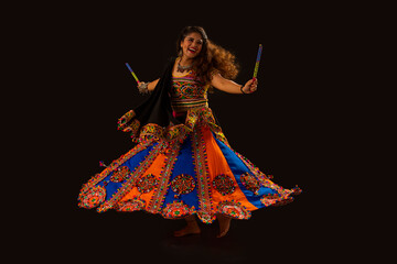 Gujarati woman dancing with dandiya sticks on a balck background, during Navratri Celebrations