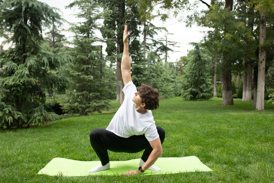 Man doing yoga in the park on the sunny morning. Fit young man exercising outdoors on yoga mat Healthy and active lifestyle concept. Training outdoors. 