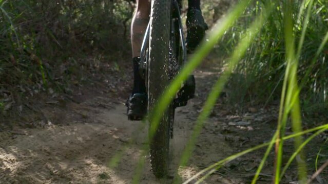 Sand flies of backwheel in slowmotion as rider pedals uphill. Closeup, behind