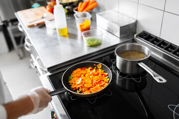 cooking food, profession and people concept - close up of male chef with frying pan stewing vegetables at restaurant kitchen