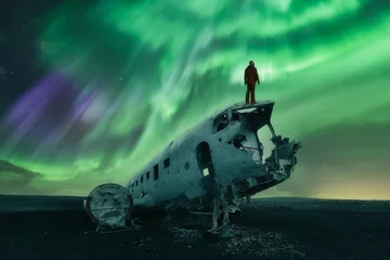 Fototapeten A man with a lantern is watching the Northern Lights (Aurora Borealis) over a Douglas DC-3 Plane wreckage. Cold night, with starry sky and polar lights over abandoned plane. Solheimasandur, Iceland © Revive Photo Media