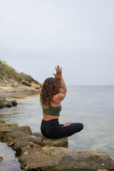 Woman practicing yoga by the sea on the rocks