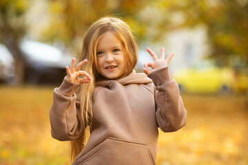 Happy little child girl laughing and playing in the autumn on the nature walk over fallen leaves outdoors. Autumn season. Happy child over nature background at city street.