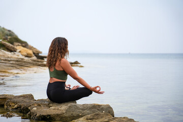Woman practicing yoga by the sea on the rocks. Padmasana - Lotus pose - meditation sitting - chin mudra