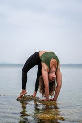 Woman practicing yoga by the sea on the rocks. Urdhva dhanurasana - Wheel pose