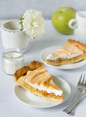 Two slices of apple pie with cinnamon and white cream on a background of coffee cups, flowers and green apples..