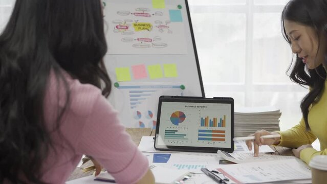 Two Asian business colleagues working together on a new project, businesswomen talking about finances, looking at patterns of markets, economies and banks.