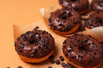 Chocolate donuts on paper on orange background, close up