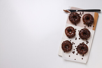 Chocolate donuts on kitchen board on white background, space for text