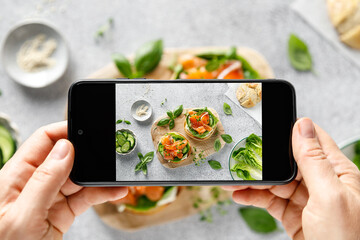 Female hands taking photo with smartphone of a healthy sandwiches with salted salmon, cream cheese,...