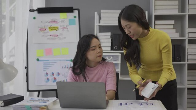 Two Asian business colleagues working together on a new project, businesswomen talking about finances, looking at patterns of markets, economies and banks.