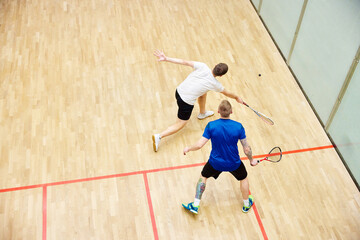 Top view of two young men, friends, sportsmen playing squash on squash court. Competition....