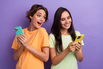 Photo of impressed funky girls dressed t-shirts online shopping modern devices isolated purple color background