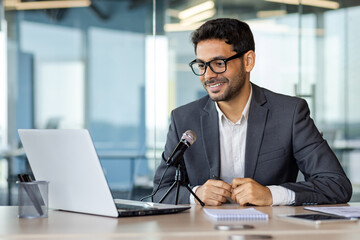Young successful business coach recording podcast audio course about success and money, man using...