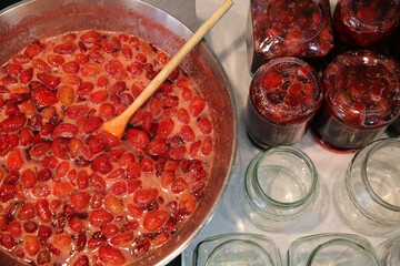 Cooking strawberry jam in a large bowl at home. Wooden spoon in a bowl with jam. Empty glass jam...