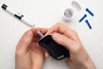 Caucasian middle aged man hands to make home testing with glucose meter over table with strips and lancets