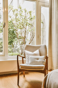 Armchair with cushion placed by window at home