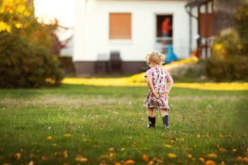 Ein kleines Mädchen mit Gummistiefeln genießt den warmen Herbsttag im Garten.