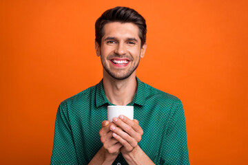 Photo of cheerful funky man dressed green shirt enjoying hot beverage isolated orange color background
