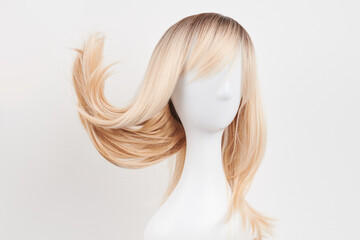 Naklejka premium Natural looking blonde wig on white mannequin head. Long hair on the plastic wig holder isolated on white background, front view.