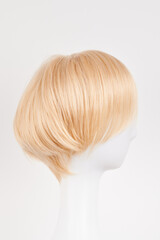Fototapeta premium Natural looking blonde fair wig on white mannequin head. Short hair cut on the plastic wig holder isolated on white background, side view.