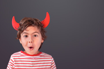 Portrait of a boy with devil horns on his head against grey background
