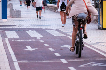 personas haciendo deporte por el paseo marítmo, en primer plano una mujer en bicicleta de espaldas - obrazy, fototapety, plakaty