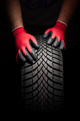 Car tire service and hands of mechanic holding new tyre on black background with copy space for text - obrazy, fototapety, plakaty