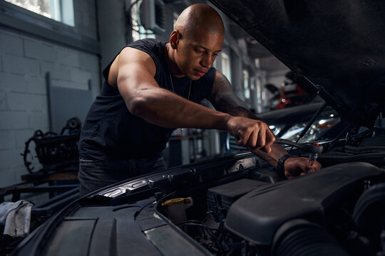 Masculine African American auto-mechanic checking sparking plugs in car
