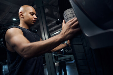 Bottom-view pumped-up black man auto-mechanic checking tire integrity