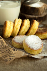 Cheesecakes on craft paper, sprinkled with powdered sugar, a glass of milk in a rustic style, dark