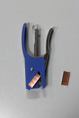 A blue stapler with a piece of copper