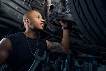 African American repairman smiling finally finding breakage on car bottom
