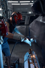 African American welder welding rusted fenders and sills of vehicle