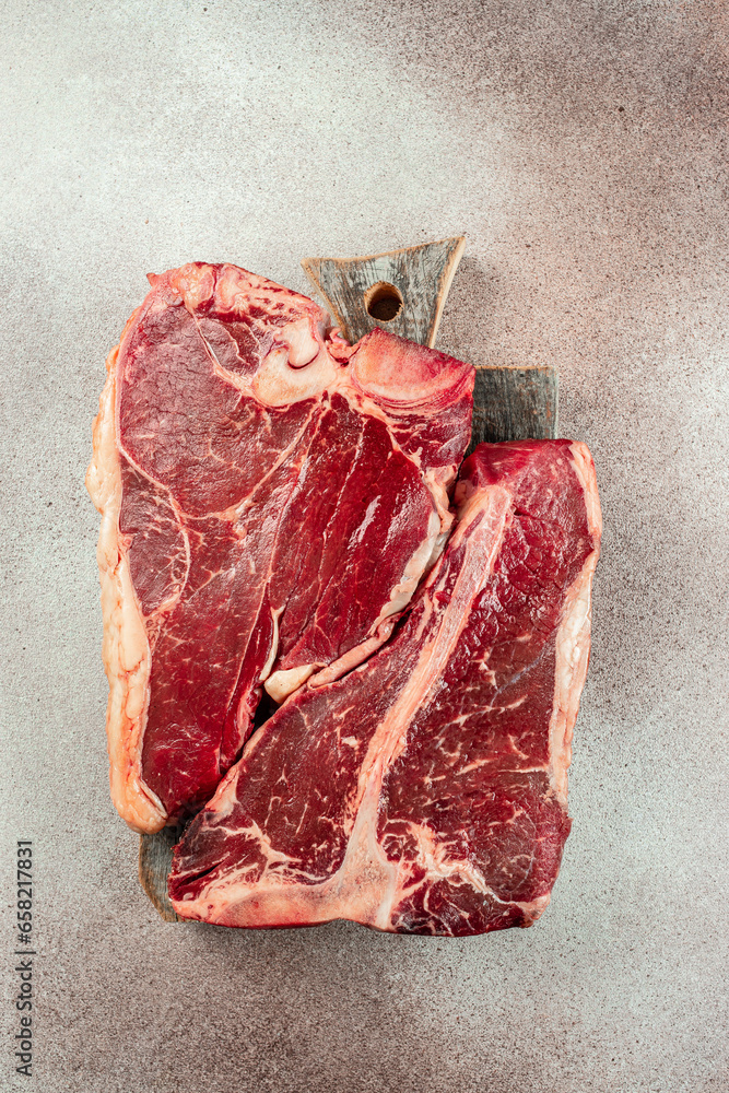 Wall mural Large raw t-bone steak on a wooden board. Porterhouse steak with a meat cleaver on a dark background. top view