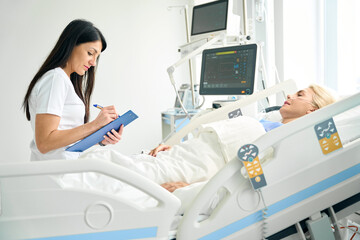 Pleasant nurse recording the patients vital signs