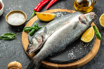 raw fish sea bass with ingredients on a dark background. banner, menu, recipe place for text, top...