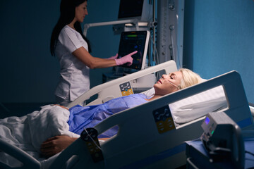 Recovering blonde lies in recovery room, nurse monitors her condition