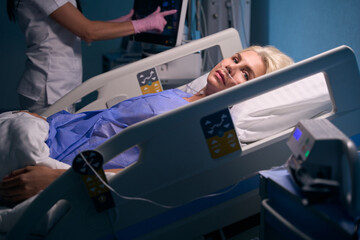 Recovering woman lies in the recovery room, medical staff monitor her condition