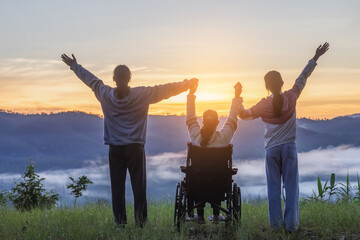 Rear view of group of family with Disabled handicapped woman sitting in wheelchair having fun together outdoors. - obrazy, fototapety, plakaty
