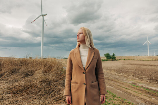 Blond woman standing in front of wind turbine under cloudy sky