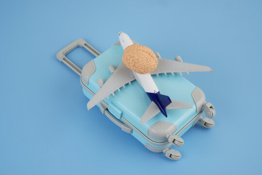 Human brain on suitcase and airplane on blue background. Brain drain concept. Copy space for text.