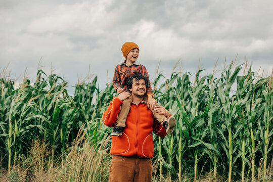 Cheerful father carrying son on shoulders in front of corn crops